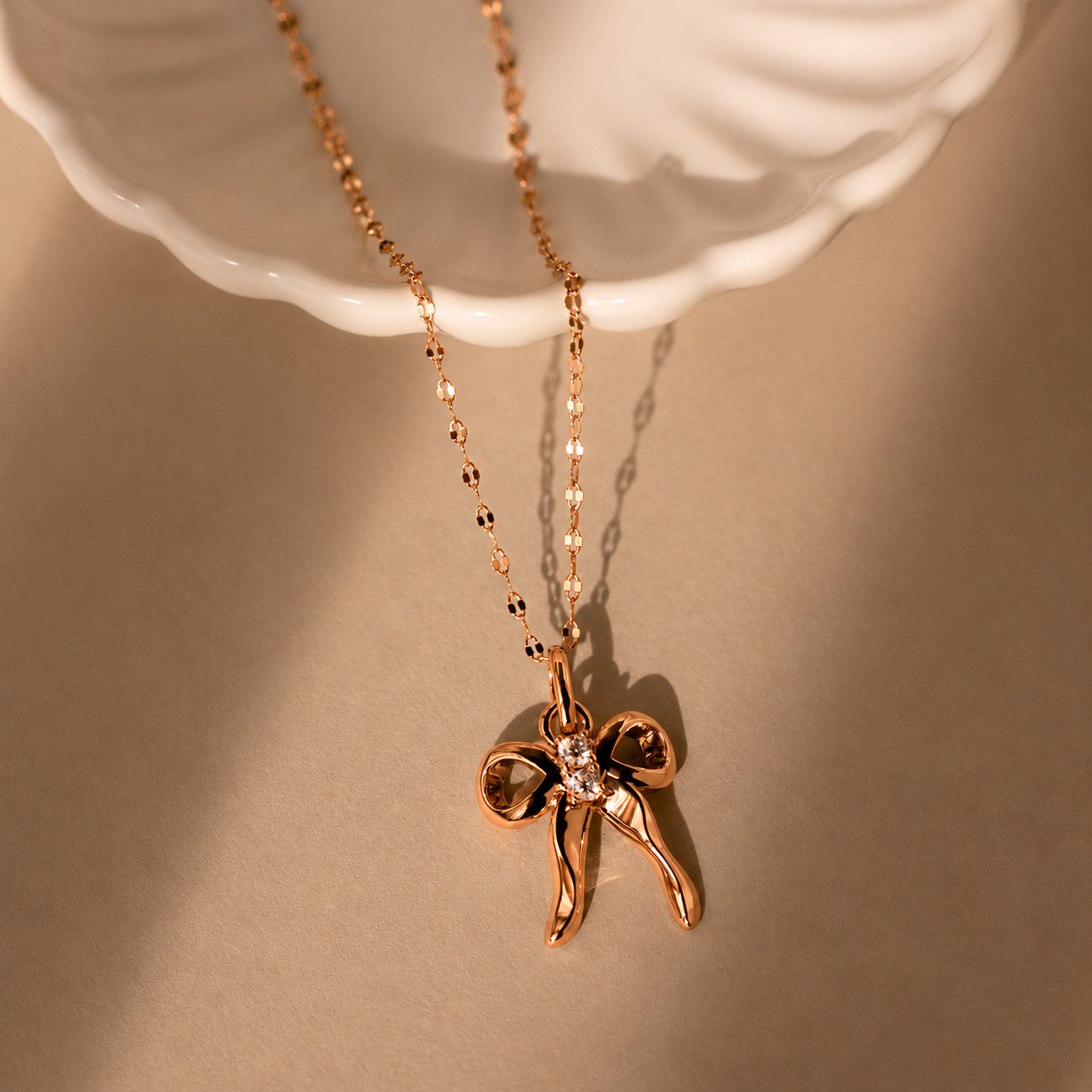Rose gold bow-shaped pendant necklace on a beige background